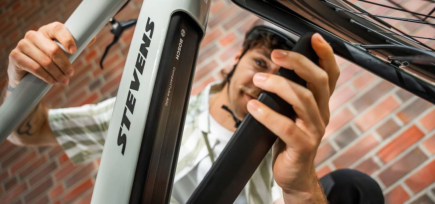 Ein Mann öffnet die Akku-Abdeckung an einem grauen Elektrorad, von schräg unten aufgenommen. 